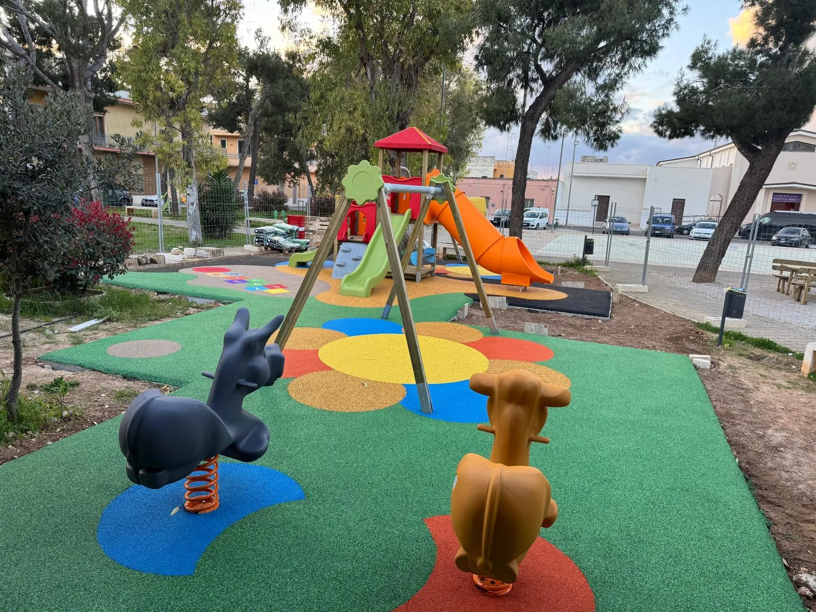 Area gioco comunale, Monteroni di Lecce. Torre con scivolo, altalene e antitrauma disegnato a corolla, sotto i pini del quartiere.